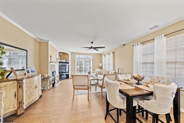 dining space featuring visible vents, ceiling fan, ornamental molding, light wood-style floors, and a fireplace