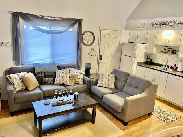 living room with sink, vaulted ceiling, and light hardwood / wood-style floors