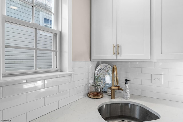 details featuring sink, white cabinets, light stone counters, and decorative backsplash