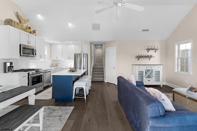 kitchen featuring vaulted ceiling, white cabinetry, a kitchen bar, a center island, and stainless steel appliances