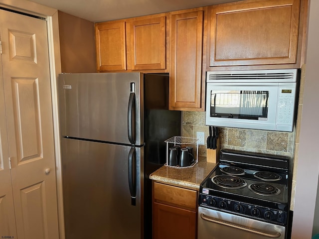 kitchen featuring electric range oven, stainless steel refrigerator, built in microwave, tasteful backsplash, and light stone countertops