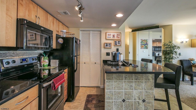 kitchen with track lighting, a kitchen breakfast bar, light carpet, and black appliances