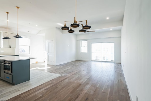 kitchen featuring stainless steel oven, vaulted ceiling, light hardwood / wood-style flooring, pendant lighting, and decorative backsplash