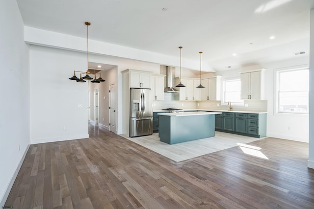 kitchen with white cabinetry, a center island, stainless steel fridge, pendant lighting, and wall chimney range hood