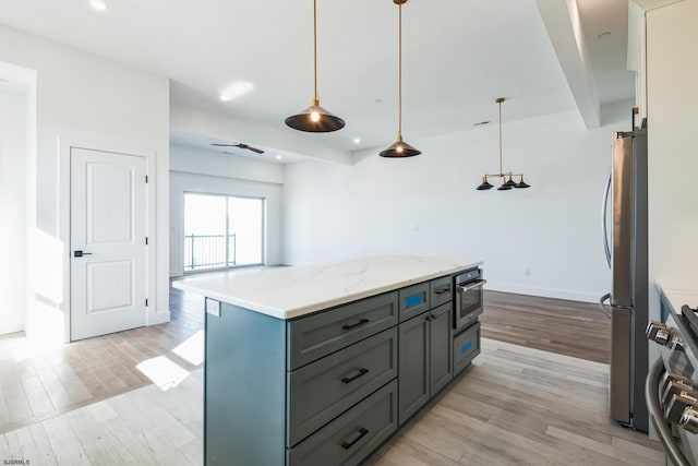 kitchen with stainless steel fridge, stove, hanging light fixtures, a kitchen island, and light wood-type flooring