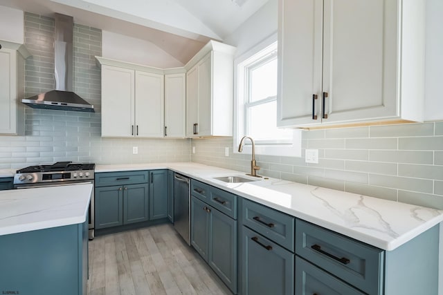 kitchen featuring sink, vaulted ceiling, white cabinets, stainless steel appliances, and wall chimney range hood