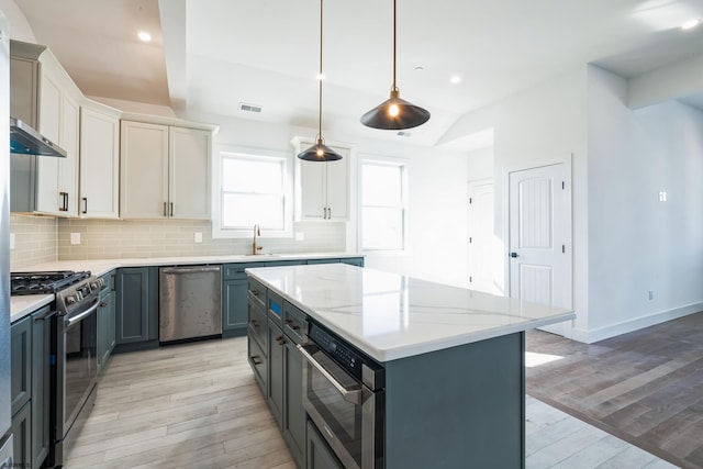 kitchen with white cabinetry, decorative light fixtures, a center island, appliances with stainless steel finishes, and light hardwood / wood-style floors