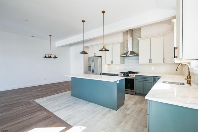 kitchen with pendant lighting, wall chimney range hood, stainless steel appliances, white cabinets, and a kitchen island