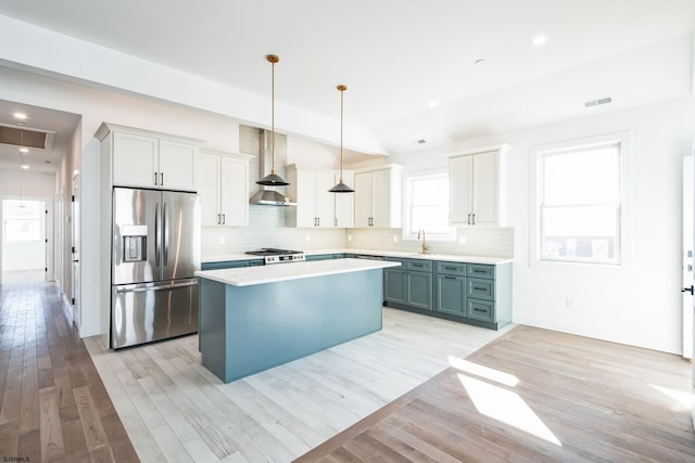 kitchen featuring pendant lighting, wall chimney range hood, light hardwood / wood-style flooring, a center island, and stainless steel fridge with ice dispenser