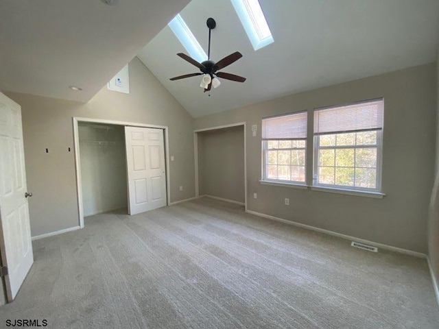 unfurnished bedroom featuring ceiling fan, a skylight, high vaulted ceiling, and light carpet