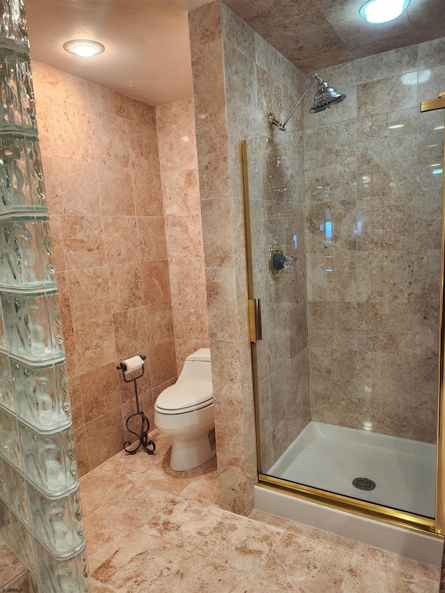 bathroom with toilet, a shower with shower door, and tile walls