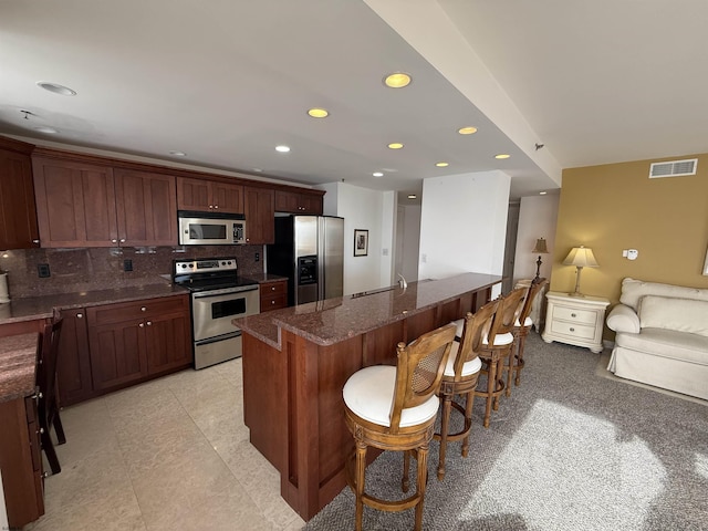 kitchen with a kitchen bar, sink, appliances with stainless steel finishes, a kitchen island with sink, and decorative backsplash