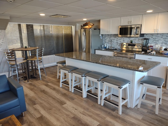 kitchen with light hardwood / wood-style flooring, a breakfast bar area, appliances with stainless steel finishes, dark stone countertops, and white cabinets