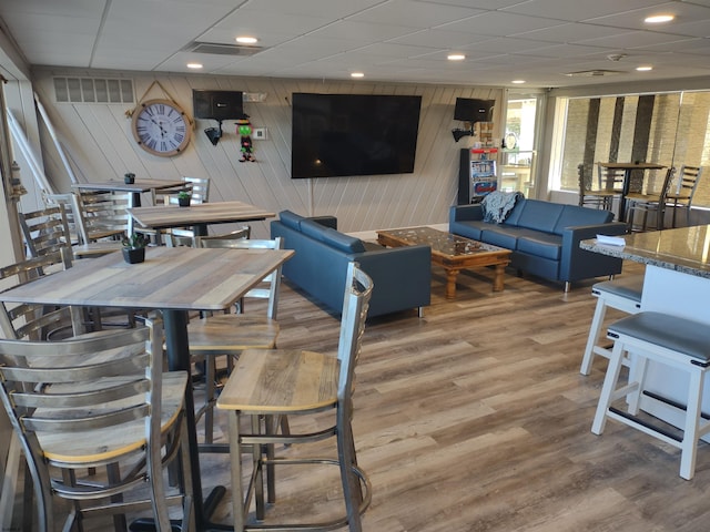 dining area featuring hardwood / wood-style flooring, a drop ceiling, and wood walls