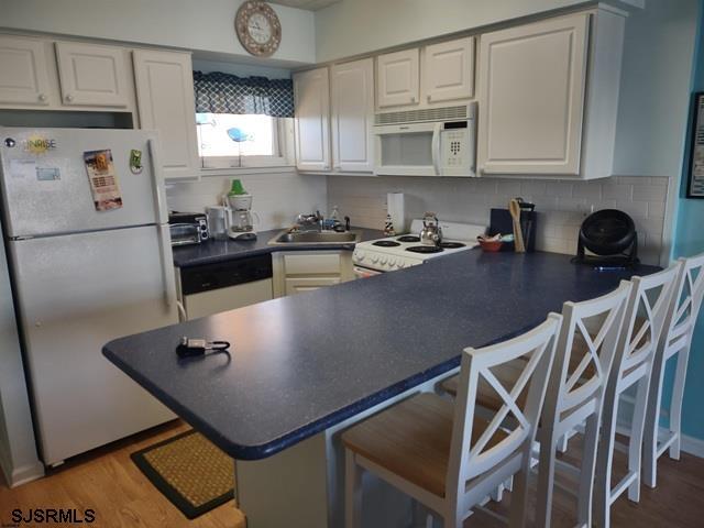 kitchen featuring sink, white appliances, kitchen peninsula, and white cabinets