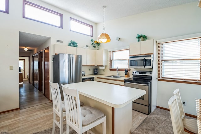 kitchen with appliances with stainless steel finishes, a towering ceiling, sink, hanging light fixtures, and light wood-type flooring