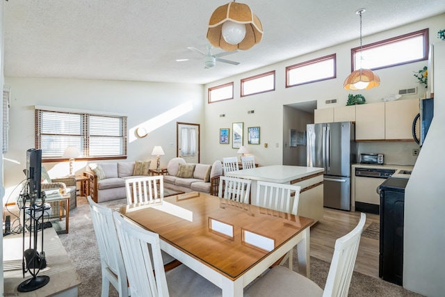 dining room with ceiling fan, a towering ceiling, a textured ceiling, and light hardwood / wood-style flooring