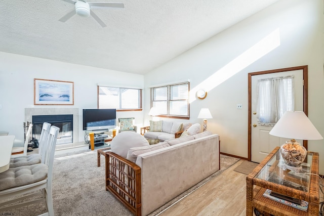 living room featuring light hardwood / wood-style flooring, a tile fireplace, ceiling fan, a textured ceiling, and vaulted ceiling