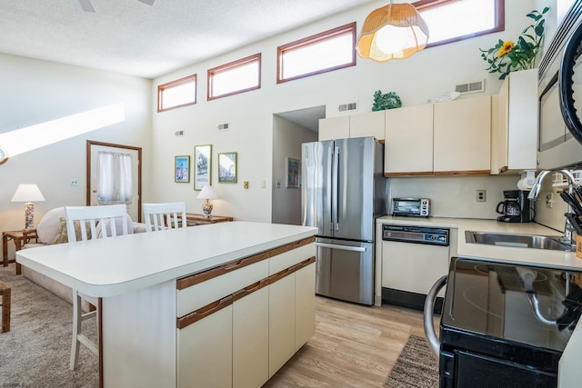 kitchen featuring sink, light wood-type flooring, appliances with stainless steel finishes, pendant lighting, and a high ceiling