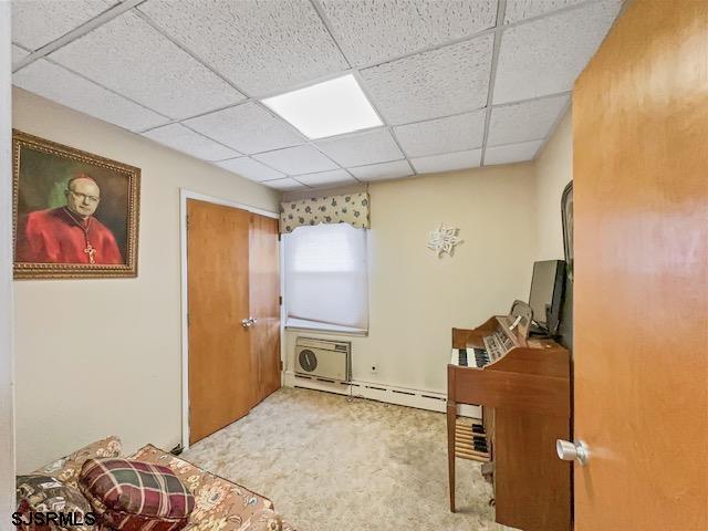 carpeted home office featuring baseboard heating, a wall mounted AC, and a drop ceiling