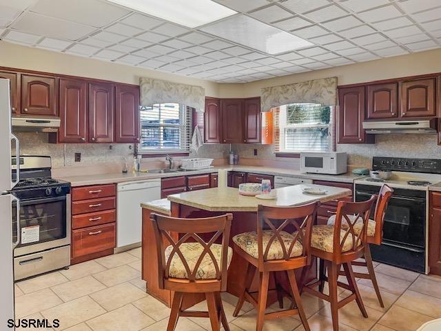 kitchen with sink, white appliances, a breakfast bar area, a paneled ceiling, and a kitchen island