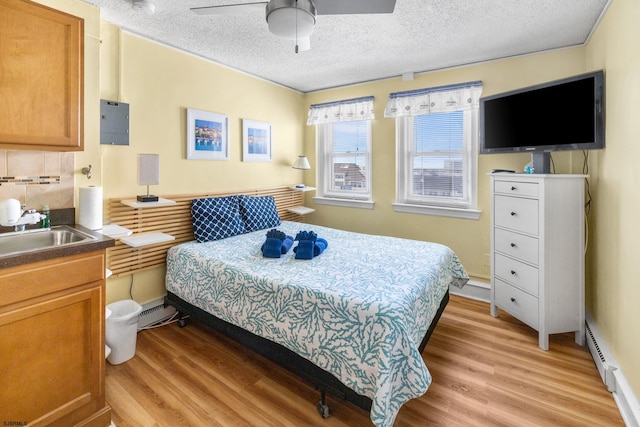 bedroom with sink, light wood-type flooring, ceiling fan, and a baseboard heating unit