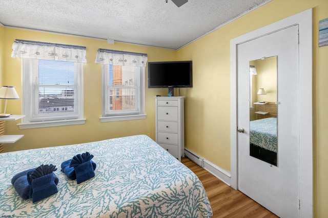 bedroom featuring baseboard heating, ceiling fan, wood-type flooring, and a textured ceiling