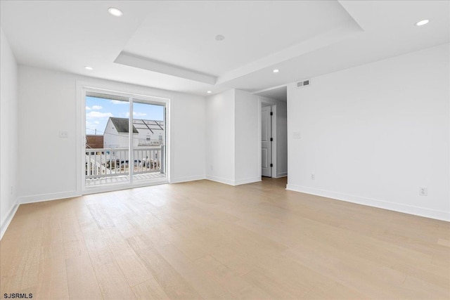 spare room with a raised ceiling and light hardwood / wood-style floors