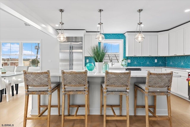 kitchen with white cabinetry, stainless steel built in refrigerator, a breakfast bar, and pendant lighting