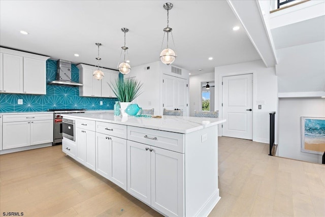 kitchen with decorative light fixtures, white cabinets, a center island, light stone countertops, and wall chimney exhaust hood