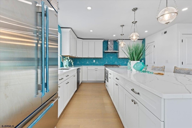 kitchen with a kitchen island, white cabinets, stainless steel appliances, light stone countertops, and wall chimney range hood