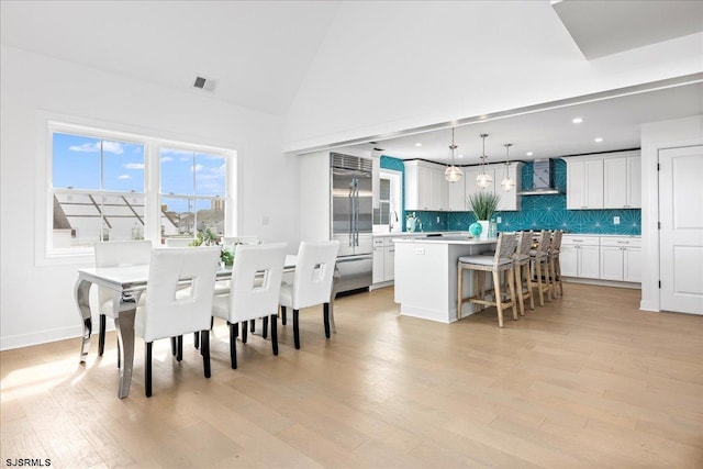 dining room featuring high vaulted ceiling and light hardwood / wood-style flooring