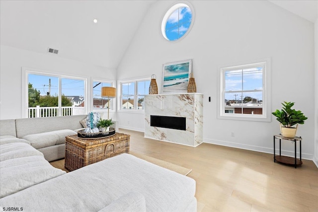 living room featuring plenty of natural light, a fireplace, high vaulted ceiling, and light wood-type flooring