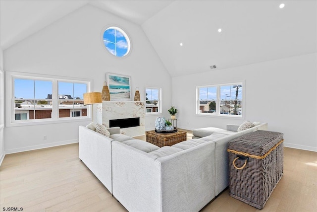 living room with light hardwood / wood-style flooring, a wealth of natural light, high vaulted ceiling, and a premium fireplace