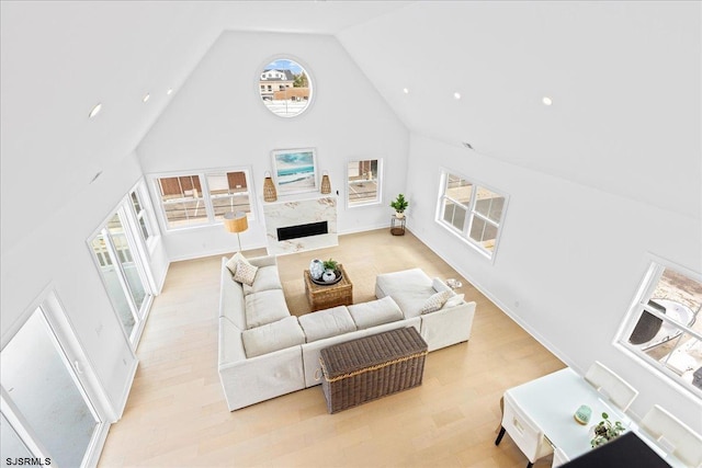 living room featuring a high end fireplace, high vaulted ceiling, and light hardwood / wood-style floors