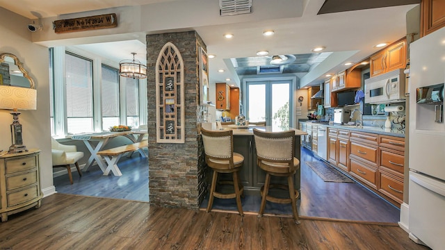 kitchen with a breakfast bar, french doors, dark wood-type flooring, white appliances, and wall chimney exhaust hood