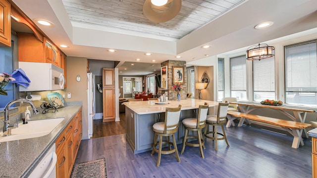 kitchen with dark wood-type flooring, sink, a breakfast bar area, wood ceiling, and a kitchen island