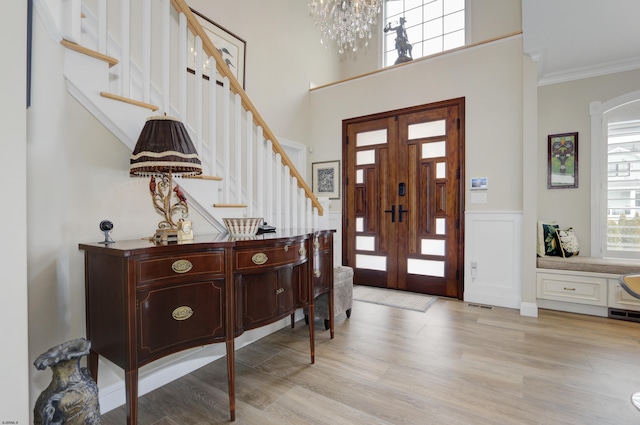 entryway featuring crown molding, a healthy amount of sunlight, a chandelier, and light hardwood / wood-style floors