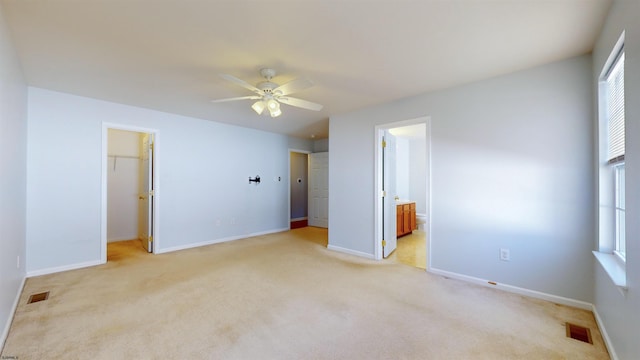 unfurnished bedroom featuring connected bathroom, a walk in closet, light carpet, a closet, and ceiling fan