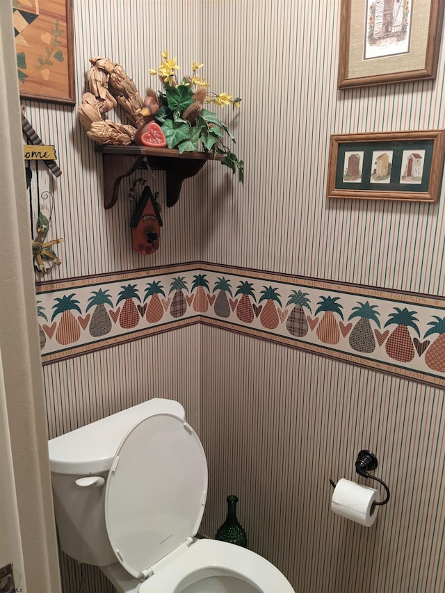 bathroom with wainscoting, toilet, and wallpapered walls