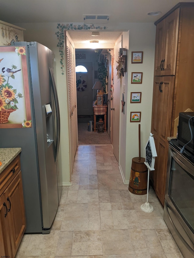 kitchen featuring visible vents, baseboards, stainless steel refrigerator with ice dispenser, arched walkways, and stone finish floor