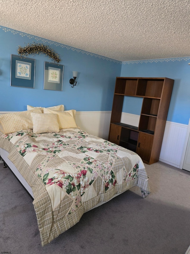 carpeted bedroom featuring a textured ceiling and wainscoting