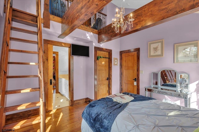 bedroom with beam ceiling, a high ceiling, a chandelier, and light wood-type flooring