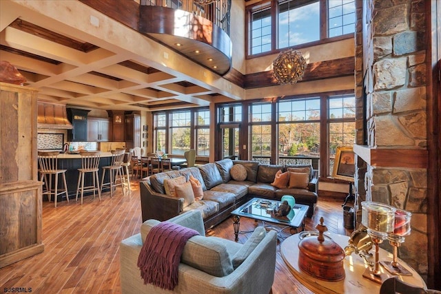 living room featuring coffered ceiling, light hardwood / wood-style flooring, a notable chandelier, beamed ceiling, and a high ceiling