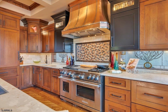 kitchen with decorative backsplash, custom exhaust hood, range with two ovens, light stone countertops, and light wood-type flooring