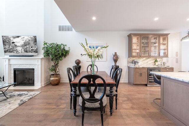 dining space with bar area, beverage cooler, light hardwood / wood-style floors, and a stone fireplace