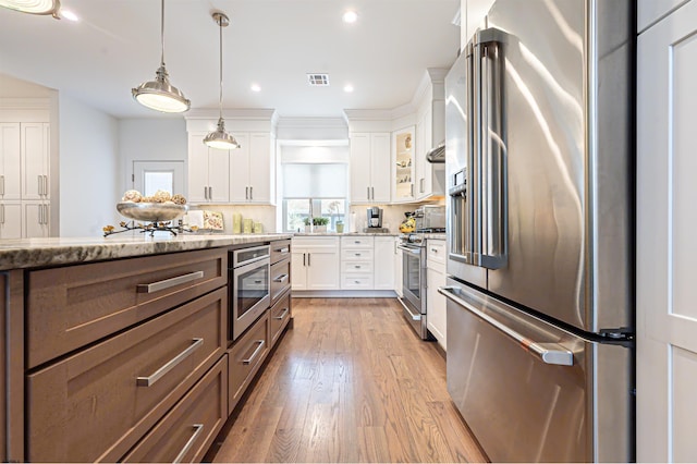 kitchen with pendant lighting, hardwood / wood-style flooring, appliances with stainless steel finishes, white cabinetry, and light stone counters