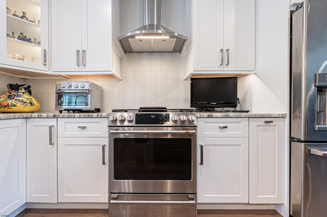 kitchen with tasteful backsplash, light stone counters, wall chimney range hood, stainless steel appliances, and white cabinets