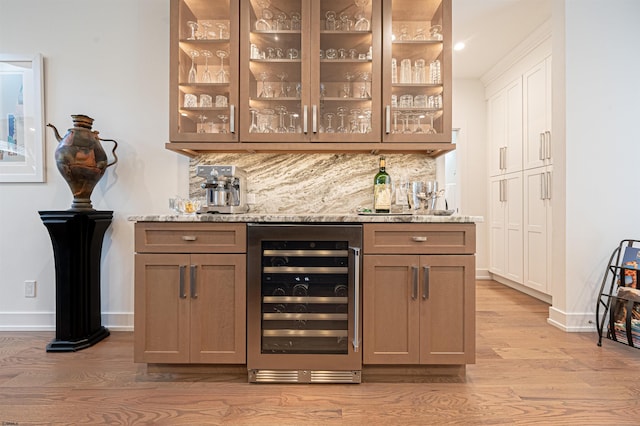 bar featuring light stone counters, beverage cooler, light hardwood / wood-style floors, and decorative backsplash