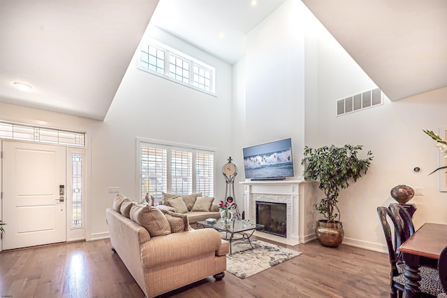 living room with a towering ceiling, a stone fireplace, and hardwood / wood-style floors